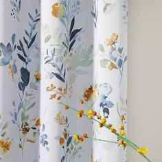 a vase filled with yellow flowers sitting next to a white curtain covered in floral print