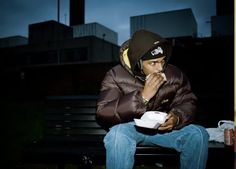 a man is sitting on a bench eating something out of a white bowl in front of him