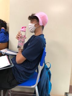 a man sitting at a desk wearing a face mask and holding a water bottle in front of him