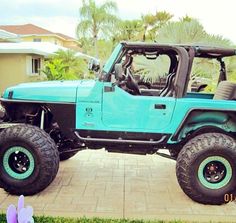 a blue jeep parked in front of a house with large tires on it's wheels