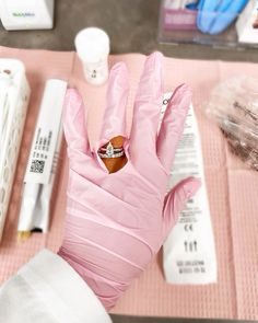 a pink gloved hand with a ring on it next to other items and pens