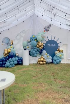 an outdoor event with blue and gold balloons on the grass, under a white tent