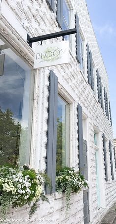 a white brick building with flowers in the window boxes and a sign that says bloom