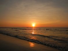 the sun is setting over the ocean and people are in the water at the beach