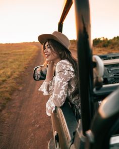 a woman wearing a hat is sitting in the back of a vehicle on a dirt road