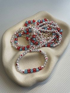 two bracelets with red, white and blue beads sitting on top of a pillow