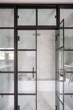 an open glass door leading to a bathroom with marble walls and flooring in the background