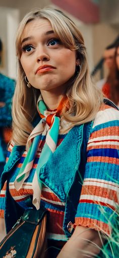 a woman with long blonde hair wearing a blue shirt and striped scarf around her neck