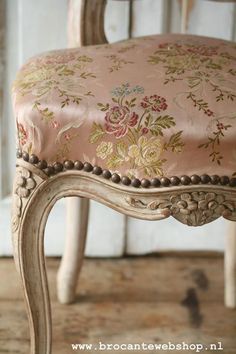 an antique chair with pink and gold fabric on it's seat, in front of a white door