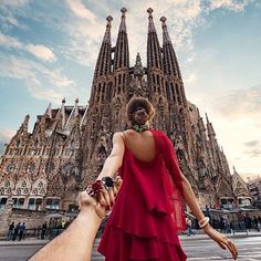 a woman in a red dress holding the hand of a man in front of a tall building