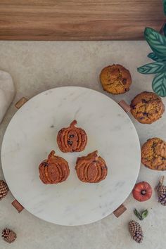 three muffins sitting on top of a white plate next to some pine cones