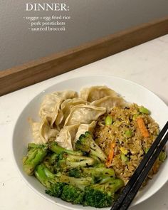 a white bowl filled with broccoli and rice next to chopsticks on a counter