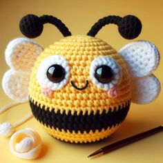 a crocheted bee with big eyes sitting on a table next to knitting needles