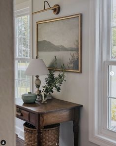 a wooden table with a lamp on top of it next to a painting and basket