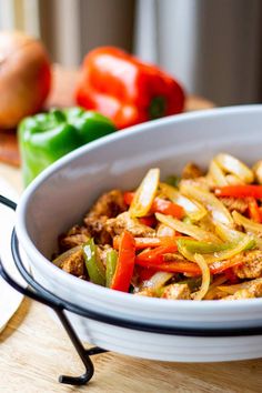 a white bowl filled with meat and vegetables on top of a wooden table next to green peppers