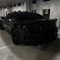 a black sports car parked in a parking garage with its hood up and lights on