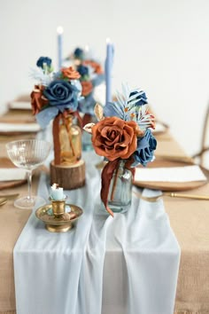 the table is set with blue and orange flowers in vases, candles, and napkins