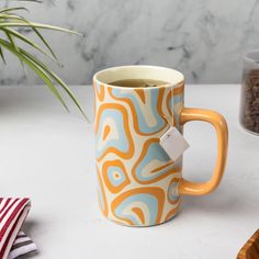 a coffee mug sitting on top of a table next to a bowl of nuts and a potted plant