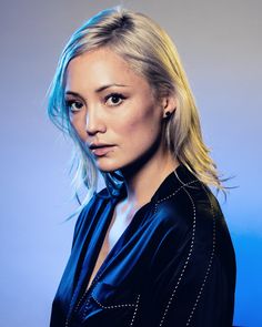 a woman with blonde hair and blue eyes posing for a photo in front of a gray background