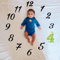 a baby laying in front of a clock with numbers on it