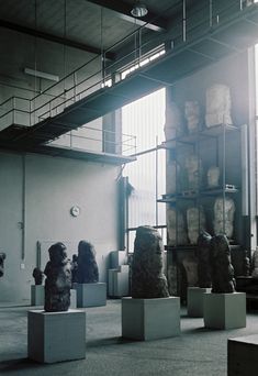 several sculptures are on pedestals in an empty room with large windows and stairs leading up to the second floor