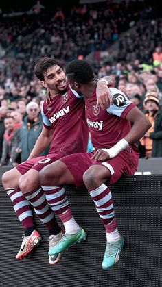 two soccer players are sitting on the back of a bench in front of an audience