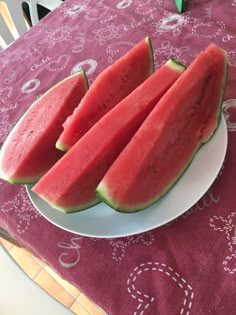 four slices of watermelon on a white plate sitting on a pink tablecloth