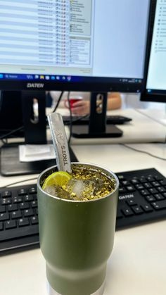 a green cup filled with liquid sitting on top of a desk next to a keyboard