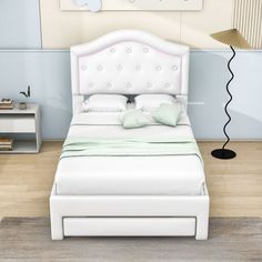 a white bed sitting in a bedroom on top of a hard wood floor next to a lamp