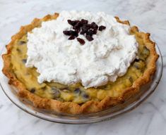 a pie topped with whipped cream and raisins on a glass plate sitting on a marble counter top