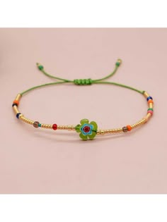 the bracelet is decorated with beads and flowers on green string, which are attached to a gold - plated cord