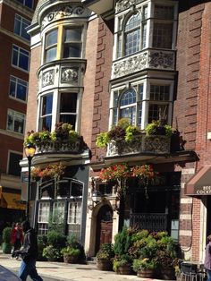 people walking down the street in front of some buildings with flower boxes on each window