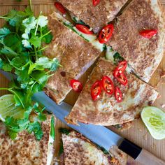 a cutting board topped with sliced up pizzas next to a knife and cilantro