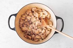 a pot filled with meat and vegetables on top of a white counter next to a wooden spoon