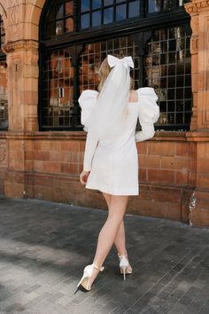 a woman in a white dress is walking down the street with her back to the camera