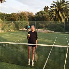 a woman holding a tennis racquet on top of a tennis court with palm trees in the background