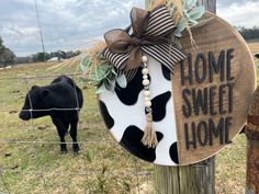 a cow standing next to a fence with a home sweet home sign hanging on it's side