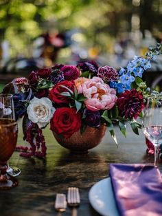 an arrangement of flowers in a basket on a table with wine glasses and napkins