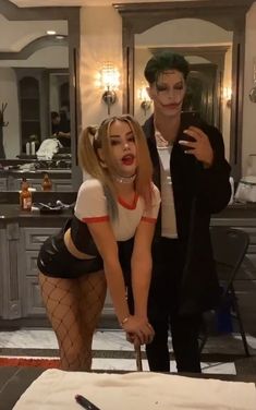 a man and woman dressed up as the joker and catwoman in a kitchen with a knife