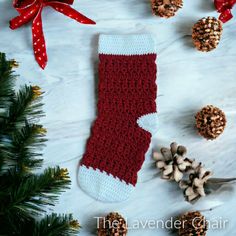 a red and white crocheted christmas stocking next to pineconi cones