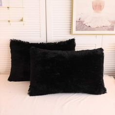 two black pillows sitting on top of a white bed next to a framed photo and an art piece