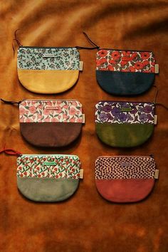 six different colored purses sitting on top of a brown cloth covered table next to each other