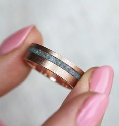 a hand holding a gold ring with blue opal inlays on the side