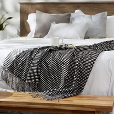 a bed with white sheets and black and white blankets on top of the headboard