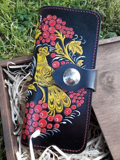 a black and red wallet with yellow flowers on it sitting in grass next to a wooden box