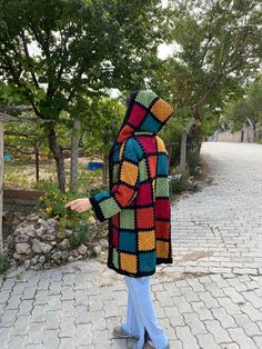 a person wearing a multicolored crocheted jacket pointing at something in the distance