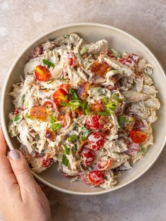 a white bowl filled with pasta salad on top of a marble counter next to a person's hand