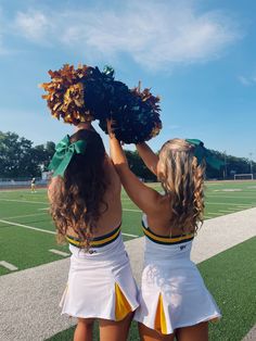 two girls in cheerleader outfits holding up pom - poms on a football field