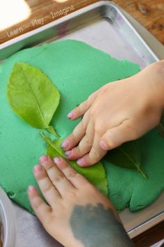 a child's hands on top of a green leaf covered dough with sprinkles