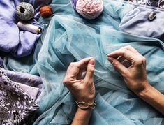 a woman is working on some fabric with scissors and knitting needles in front of her